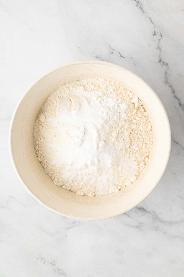 A white bowl filled with a mixture of flour and baking powder sits on a light marble surface.