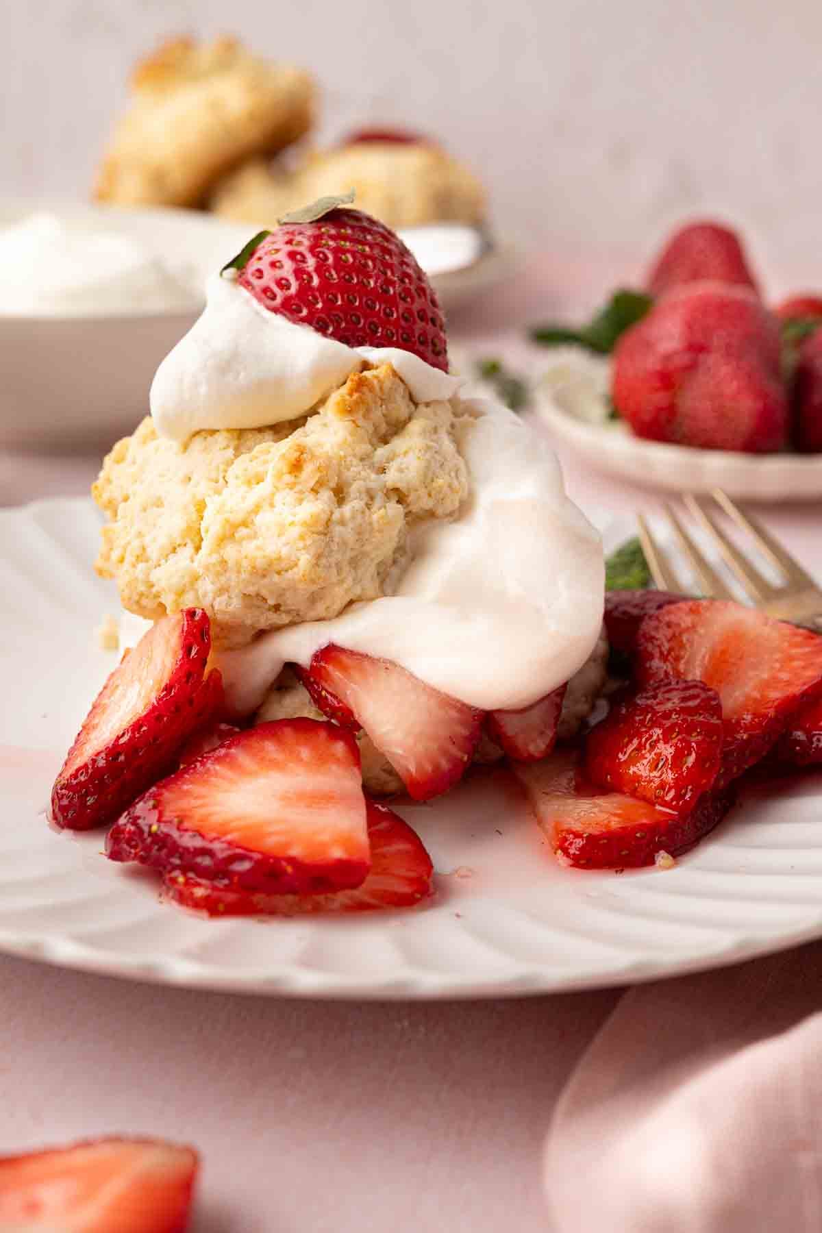 A plate of strawberry shortcake with sliced strawberries, whipped cream, and a biscuit, garnished with a halved strawberry.