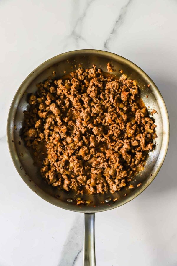 A skillet filled with cooked and seasoned ground beef sits on a white marble surface.