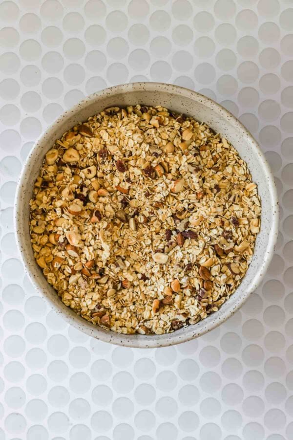 A bowl filled with a mixture of chopped nuts and oats sits on a white, textured surface.