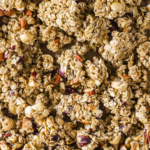 Close-up of maple pecan granola clusters with oats and nuts. Text at the top reads "Maple Pecan Granola"; website lenaskitchenblog.com at the bottom.