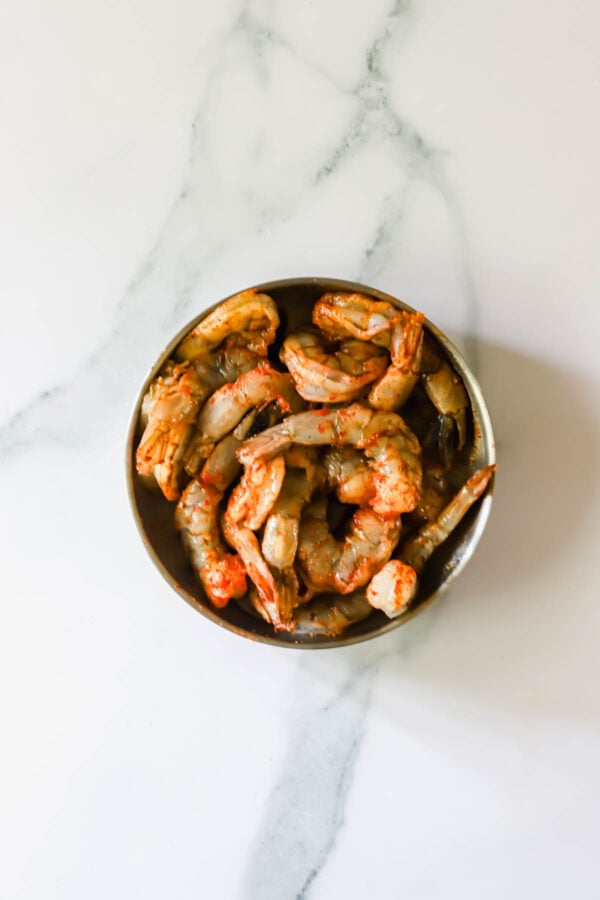 A metal bowl filled with uncooked, deveined shrimp sits on a white marble surface.