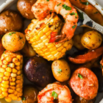 A plate of sheet pan shrimp boil with shrimp, corn on the cob pieces, baby potatoes, and sliced sausage, garnished with herbs.