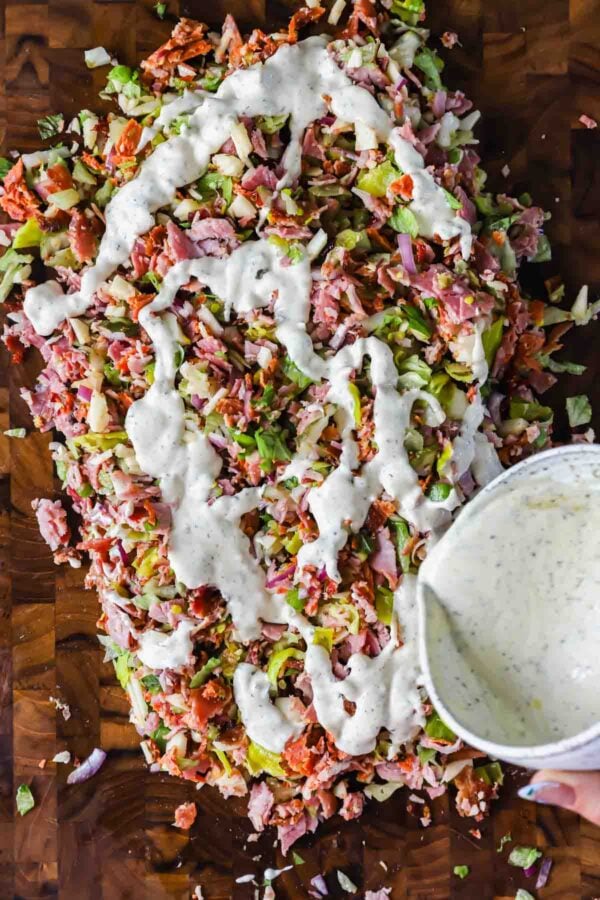 Chopped salad ingredients on a wooden surface with creamy dressing being poured over the top.