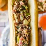 A hand holds a chopped sandwich filled with a mixture of meats, vegetables, and cheese in a hot dog bun. Text reads "Best Chopped Sandwich Recipe" and "LenasKitchenBlog.com.