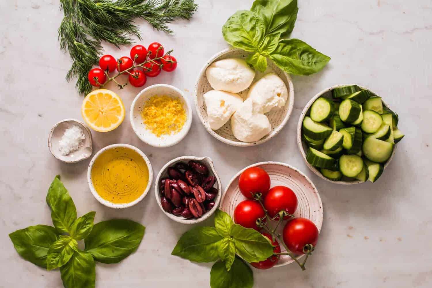 individual white bowls with vegetables, oil, lemon, and cheese with green herbs on the side