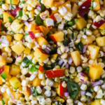Close-up of corn and peach salad with chopped red onion, cilantro, and red pepper, displayed on a white platter.