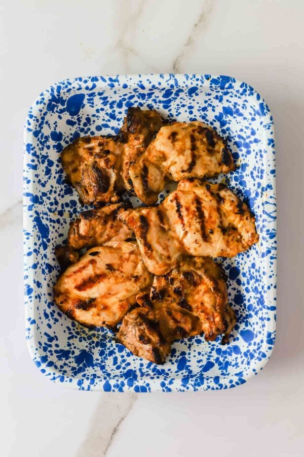 Grilled chicken pieces arranged on a blue and white splatter-patterned rectangular tray, placed on a light-colored surface.