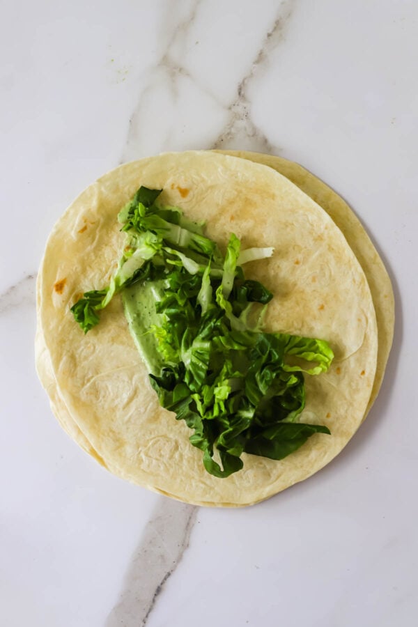 Two flour tortillas stacked on a white surface, topped with chopped leafy greens.