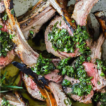 Sliced grilled rack of lamb topped with a green herb sauce, arranged on a plate.