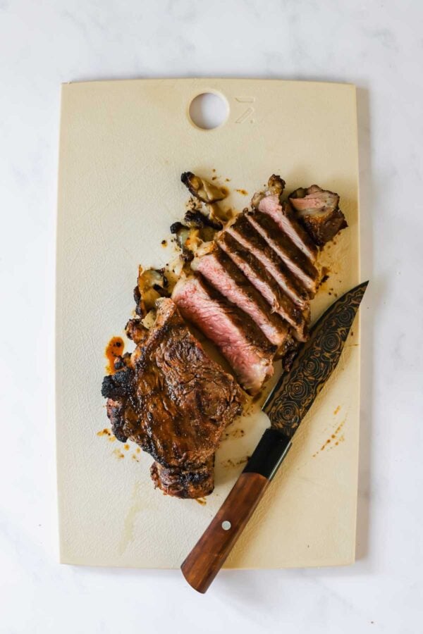 Sliced cooked steak on a white cutting board with a knife beside it.