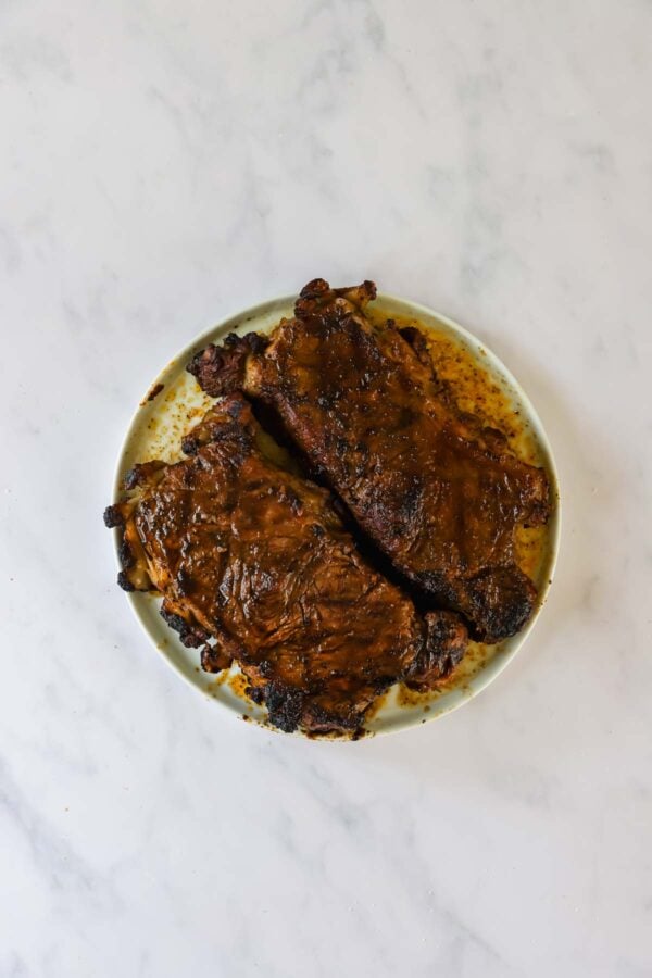 Two cooked steaks on a round white plate, photographed from above on a marble surface.