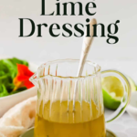 A glass pitcher of honey lime dressing with a spoon sits on a plate, next to a sliced lime and salad greens. Text reads: "The Best Honey Lime Dressing.