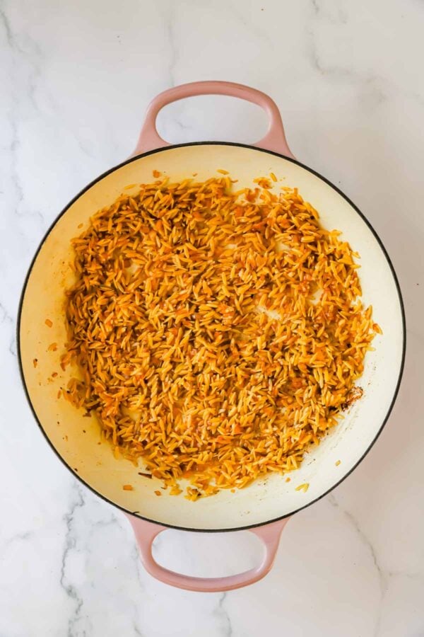 Large pot with cooked, orange-tinted rice evenly spread inside, resting on a white marble surface.