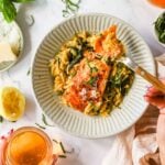 A plate of orzo pasta with cooked salmon and greens, garnished with herbs, next to a drink, lemon half, and a small dish of grated cheese.