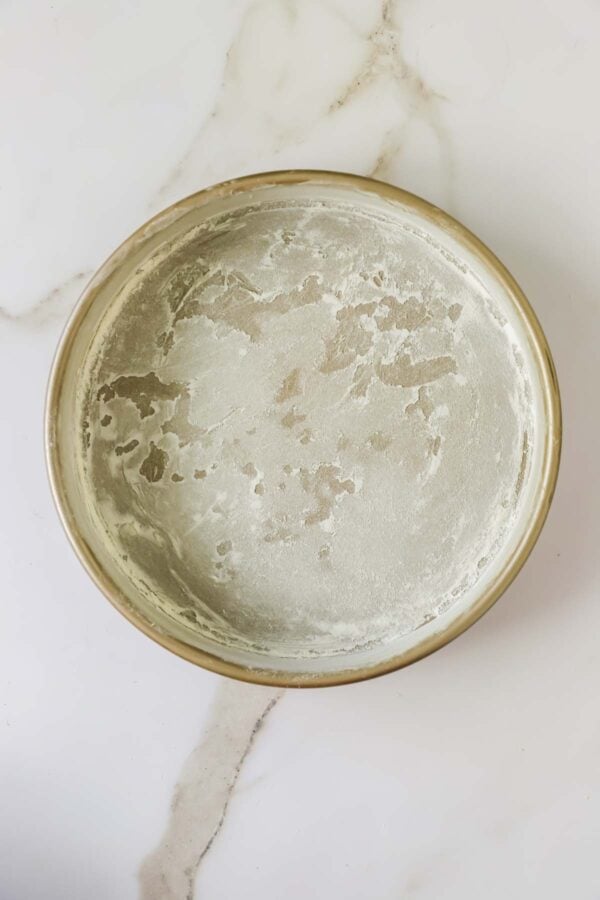A round metal cake pan with a light dusting of flour on the inside, sitting on a white marble surface.