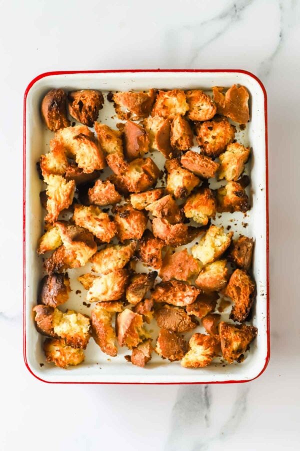 A baking dish filled with unevenly torn, toasted bread pieces on a white marble surface.