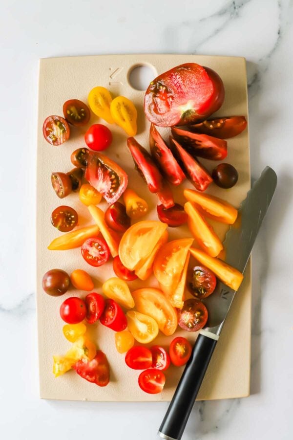 A variety of sliced and halved tomatoes are arranged on a cutting board next to a knife.