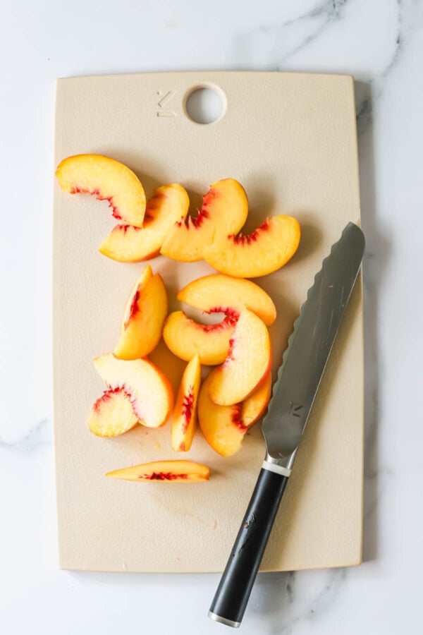 Sliced peaches arranged on a cutting board next to a serrated knife with a black handle.