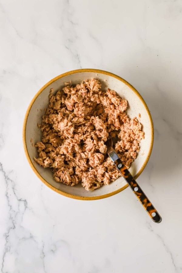 Bowl of flaked tuna with a fork on a marble surface.