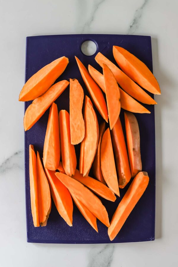 Orange sweet potato wedges arranged on a dark blue cutting board, set on a white marble surface.