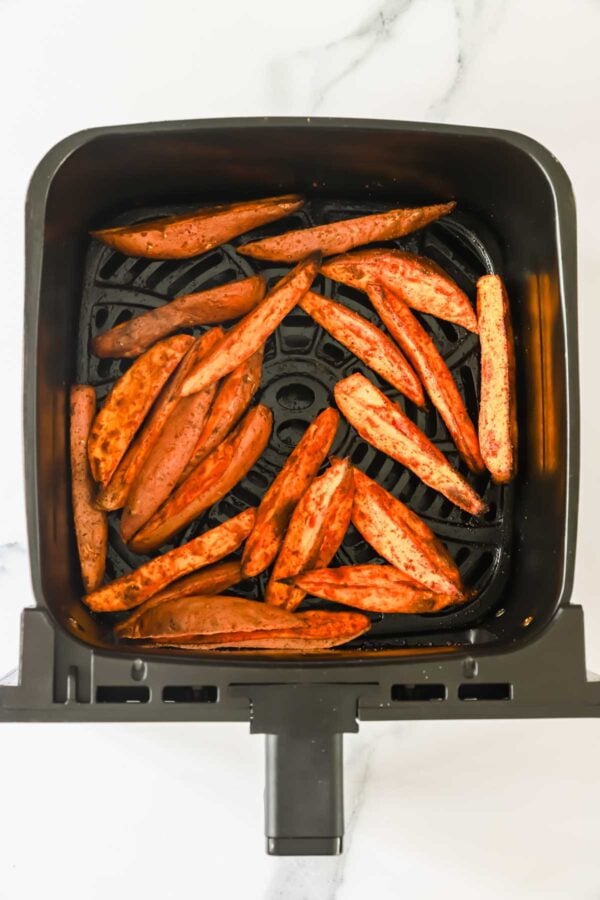 Sweet potato wedges arranged in a single layer inside an air fryer basket, ready to be cooked.
