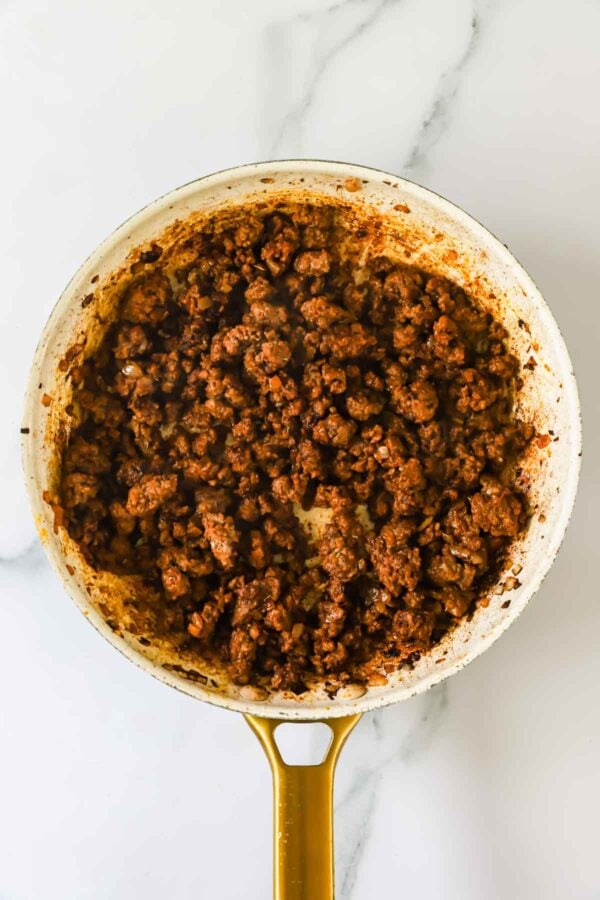 Cooked ground beef with seasoning in a white skillet on a marble surface, viewed from above.