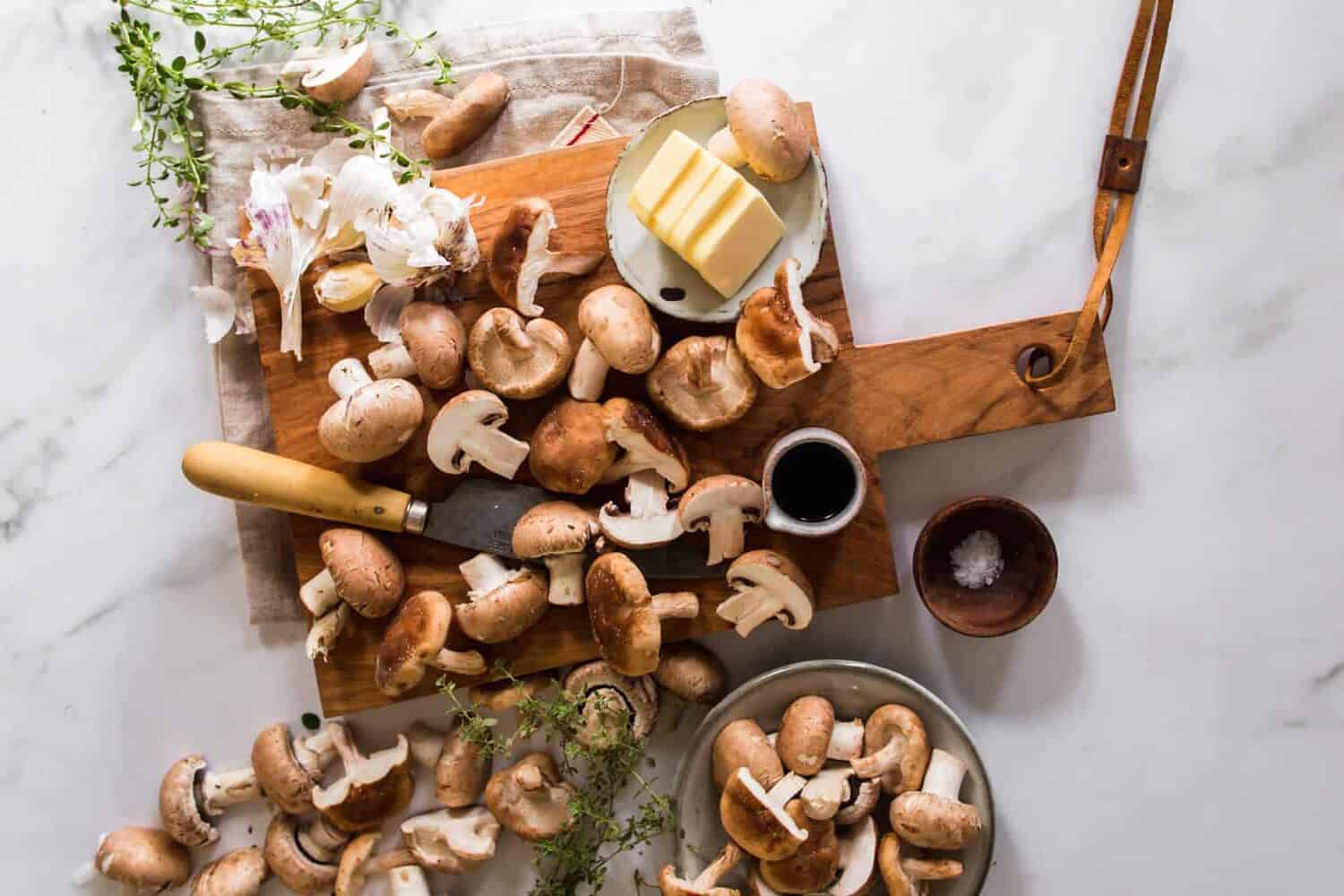 Chopped mushrooms on a cutting board. Butter and herbs on the side.