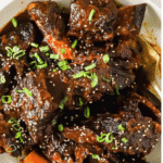 Braised beef short ribs topped with chopped green onions and sesame seeds, served in a white bowl with sauce.
