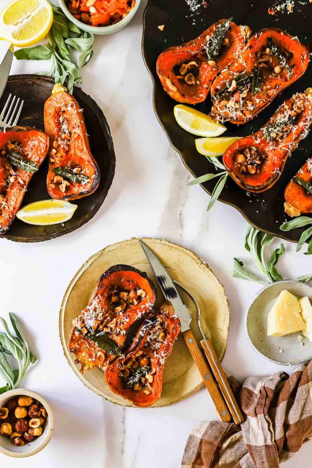 Roasted butternut squash halves topped with nuts, herbs, and cheese, served with lemon wedges.