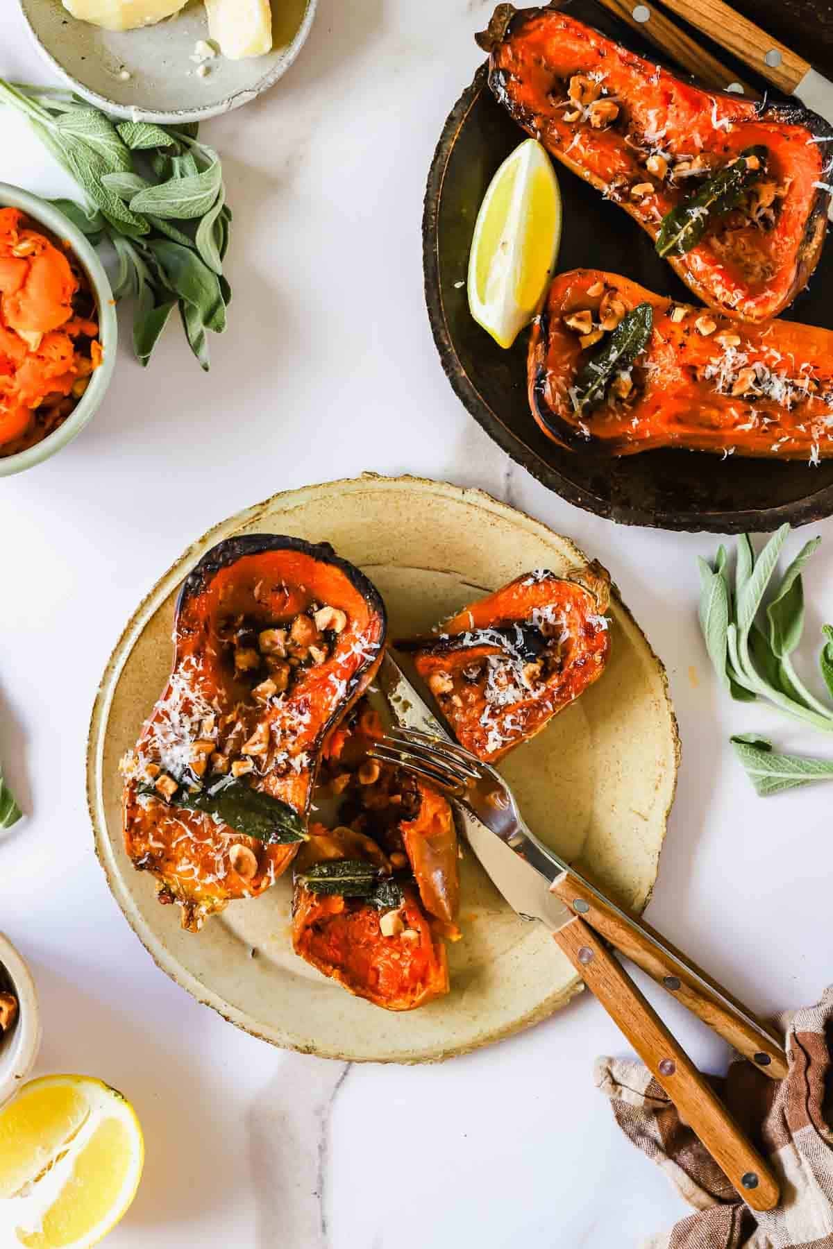 Roasted butternut squash halves topped with nuts, herbs, and cheese, served with lemon wedges.