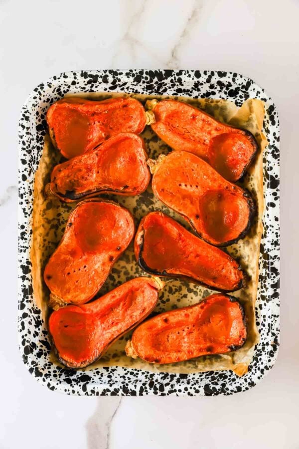 Seven halves of roasted butternut squash arranged in a speckled baking pan.