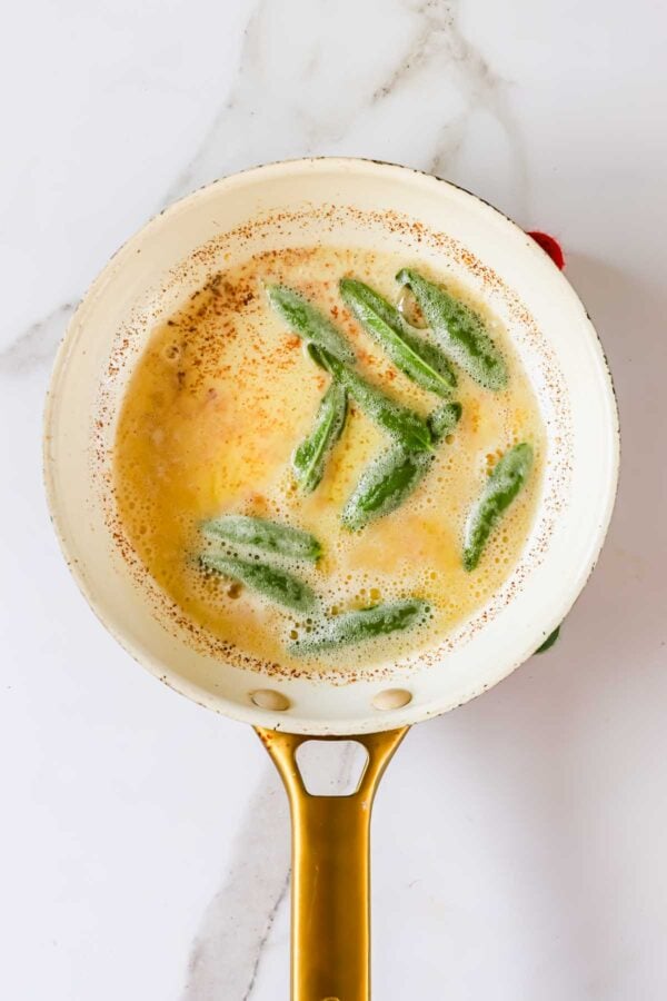 Sage leaves frying in foaming butter in a skillet.