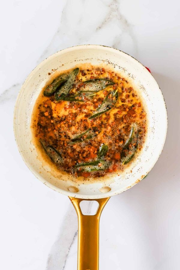 Sage leaves frying in foaming brown butter in a skillet.