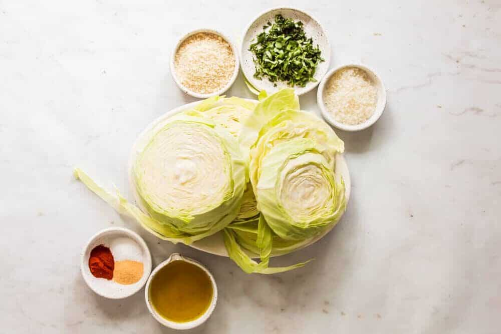 raw cabbage on a large white plate next to smaller plates holding herbs and seasonings.